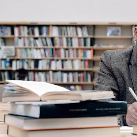 person at a library desk taking notes with books