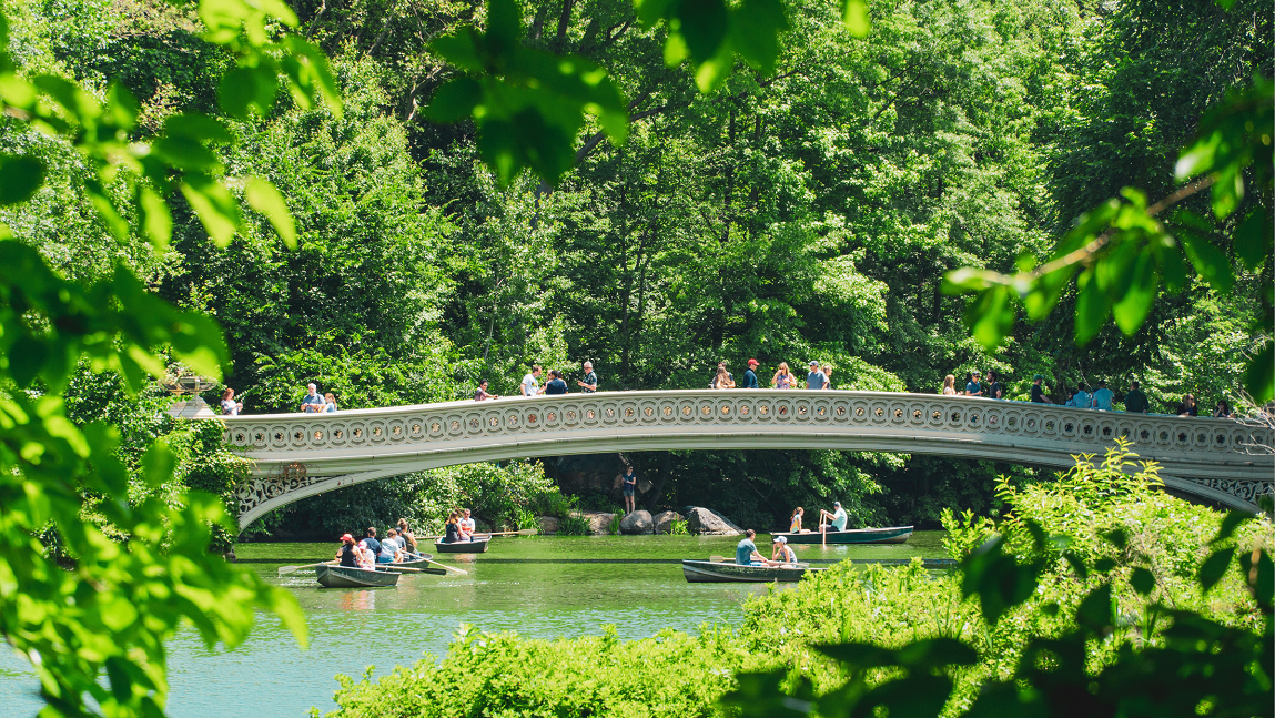 Image of bridge with pedestrians over a small body of water with small boats and passengers.