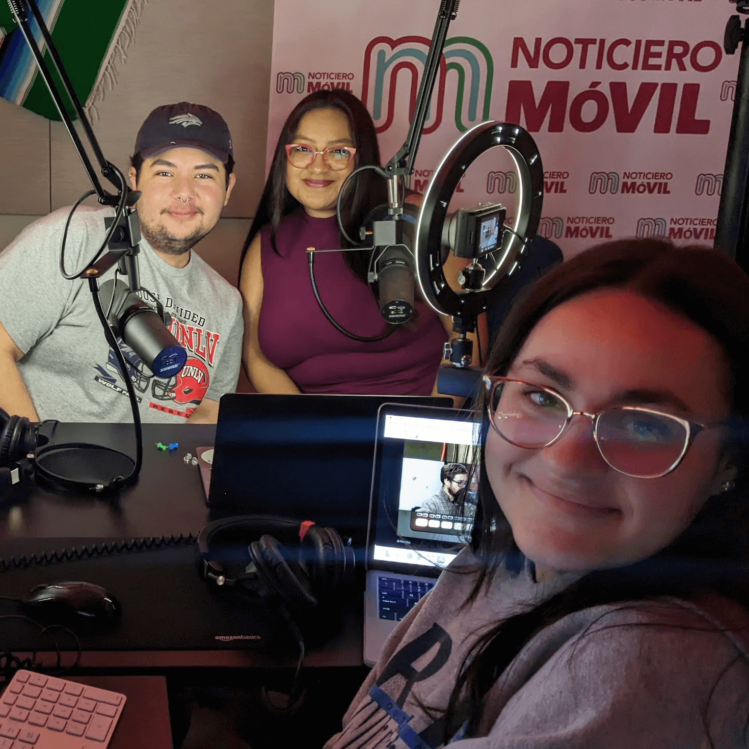 Three student reporters pose for a selfie in a dark, radio production booth.